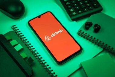 Prag, Çek Cumhuriyeti - 08 18 2025: Merkezde Airbnb logosu sergilenen bir cep telefonu ile ofis malzemeleri düzenlemesi. Airbnb dünya çapında kısa vadeli konaklama için bir platformdur..