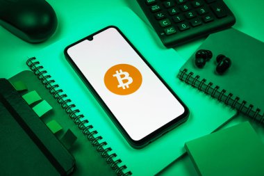 Prag, Çek Cumhuriyeti - 08 18 2025: Merkezde Bitcoin logosu sergilenen bir cep telefonu ile ofis malzemeleri düzenlemesi. Bitcoin merkezi olmayan işlemler için dijital bir kripto para birimidir.