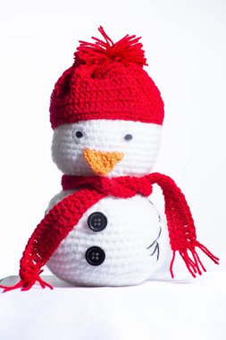 Kırmızı şapka ve eşarp takan tığ işi bir kardan adam. Kardan adamın düğmeli bir burnu ve düğmeli bir gözü var.