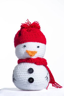 Kırmızı şapkalı ve eşarplı küçük beyaz bir kardan adam. Şapka iplikten yapılmış ve eşarp benzer bir malzemeden yapılmış. Kardan adamın neşeli ve neşeli bir görüntüsü var, sanki dışarı çıkmaya hazır gibi.