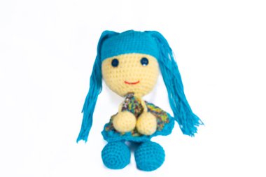 Uzun mavi saçlı mavi ve sarı bir bebek. Bebek beyaz bir arka planda oturuyor. Bebeğin yüzünde bir gülümseme var.