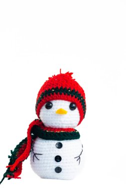 Kırmızı şapkalı ve yeşil eşarplı beyaz bir kardan adam. Şapka örülmüş ve atkı iplikten yapılmış.