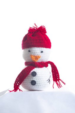 Kırmızı şapkalı ve eşarplı küçük, beyaz bir kardan adam beyaz arka planda oturuyor. Şapka kırmızı ve eşarp da kırmızı. Kardan adama neşeli ve neşeli bir görünüm veriyor.