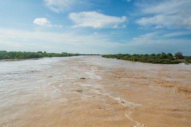 Bir nehir suyla doludur ve gökyüzü mavidir. Su kahverengi ve gökyüzü berrak.
