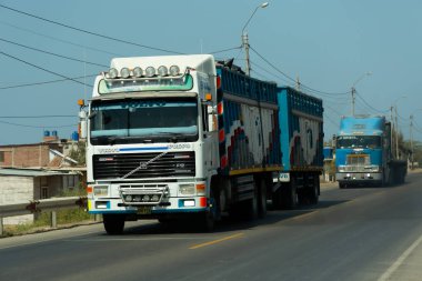 Acapulco, Tumbes, Peru 11-30-2024: otoyolda mavi römorklu beyaz Volvo F12 kamyonu. Arka planda, aynı şeritten gelen başka bir mavi kamyon daha var. Ön plandaki kamyonda 