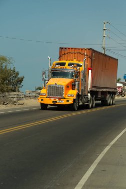 Acapulco, Tumbes, Peru 11-30-2024: Büyük turuncu bir tır yolda ilerliyor. Kamyon büyük bir konteynır taşıyor. Yol boş ve gökyüzü temiz.