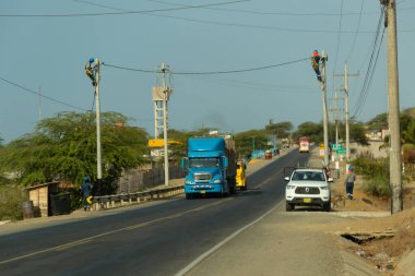 Acapulco, Tumbes, Peru 11-30-2024: Önünde beyaz bir araba olan mavi bir tır yolda ilerliyor. Kamyon büyük bir yük taşıyor.