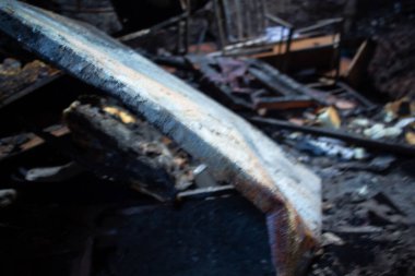 Yanmış bir araba yere yapışmış bir metal parçası ile birlikte. Araba enkaz ve küllerle çevrili. Sahne yıkım ve yıkım dolu.