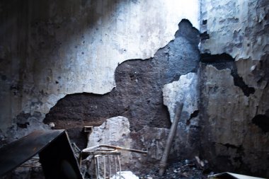 Hasarlı duvarı olan bir oda, duvarın ortasındaki delik oldukça fark edilebilir. Oda bakımsız görünüyor, enkaz etrafa saçılmış ve terk edilmişlik hissi var.