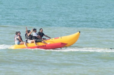 Zorritos, Tumbes, Peru - 24 Aralık 2023: Bir grup insan suda muz teknesine biniyor. Tekne sarı ve kırmızı ve insanlar can yelekleri giyiyor. Sahne eğlenceli ve maceralı, çünkü grup suda gezintiye çıkıyor..