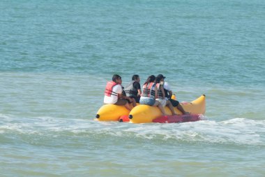 Bir grup insan okyanusta muz salına biniyor. Sal sarı ve kırmızı, ve insanlar can yelekleri giyiyor. Su dalgalı ve sal dalgaların arasında hareket ediyor..