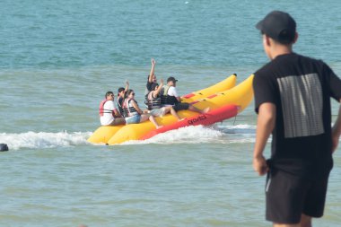 Zorritos, Tumbes, Peru - 24 Aralık 2023: Bir grup insan sarı ve kırmızı şişme bir sala biniyor. Siyah gömlekli adam kıyıdan onları izliyor..