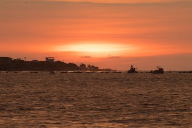 Güneş okyanusun üzerinde batıyor, suyun üzerine sıcak bir parıltı saçıyor. Gökyüzü bulutlarla dolu, sakin ve huzurlu bir atmosfer yaratıyor. Sudaki tekneler dağıtıldı.