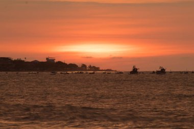 Güneş okyanusun üzerinde batıyor, suyun üzerine sıcak bir parıltı saçıyor. Gökyüzü bulutlarla dolu, sakin ve huzurlu bir atmosfer yaratıyor. Sudaki tekneler dağıtıldı.