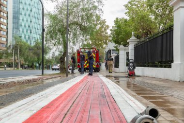 Santiago, Şili - 25 Ekim 2020: Bir itfaiye aracı caddede kırmızı ve beyaz bir çizgi üzerine park edilmiştir. İki itfaiyeci sırada bekliyor, içlerinden biri hortum tutuyor..