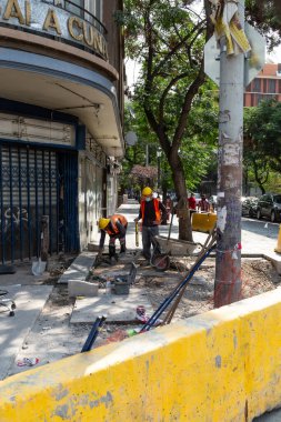 Santiago, Şili - 27 Ekim 2020: Bir grup inşaat işçisi bir binanın önündeki kaldırımda çalışıyor. İşçiler sert şapka ve turuncu yelek giyiyorlar.