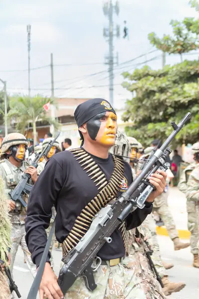 Kamuflaj üniformalı bir adam bir tüfek tutuyor ve yüzünde bir kafatası var. Askeri bir geçit töreninin bir parçası..