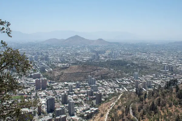 Arkasında dağ olan bir şehir manzarası. Şehir yüksek binalarla dolu ve gökyüzü açık..