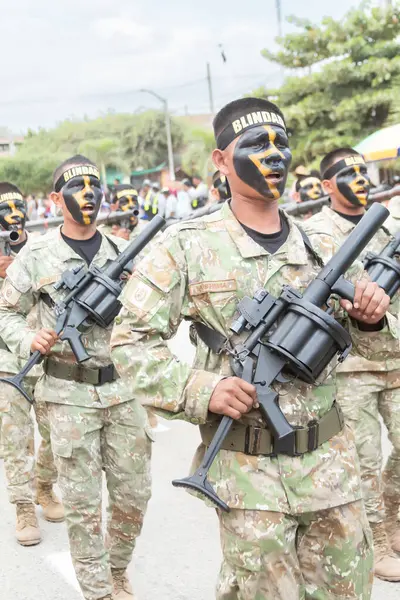 Kamuflaj üniformalı bir adam bir tüfek tutuyor ve yüzünde bir kafatası var. Askeri bir geçit töreninin bir parçası..