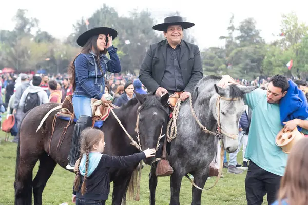 Santiago, Şili - 19 Eylül 2018: Bir adam ve bir kadın tarlada ata biniyorlar. Etraflarında bir grup insan duruyor, bazıları sepetleri tutuyor. Sahne canlı ve eğlenceli, insanlar eğleniyor gibi görünüyor..