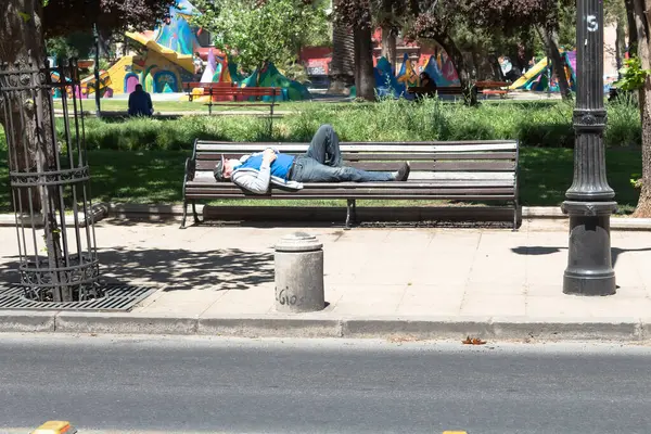 Santiago, Şili - 16 Ekim 2020: bir adam parktaki bankta uyuyor. Banka bir caddenin yanındaki kaldırımda yer alıyor..