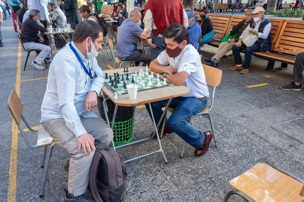 Santiago, Şili - 25 Ekim 2020: halka açık bir alanda satranç oynayan iki adam. Bir adam maske takıyor. Arka planda birkaç kişi daha var, bazıları banklarda oturuyor..