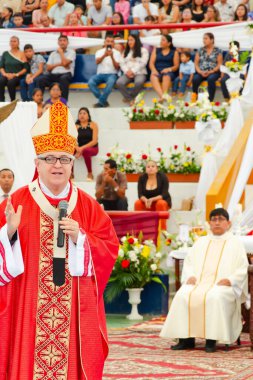 Tumbes, Tumbes, Peru 21-10-2023, Doğrulama Ayini: Kırmızı cüppeli bir adam kalabalığın önünde mikrofona konuşuyor. Adam büyük bir şapka ve gözlük takıyor. Kalabalık onu dikkatle izliyor.
