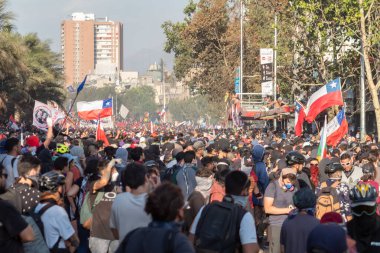 Santiago de Chile - Şili, 25-11-2019: Bir sokakta büyük bir kalabalık toplandı, bayrakları havada sallıyorlar. Bayraklar kırmızı, beyaz ve mavi olmak üzere farklı renklerdedir. Atmosfer canlı ve enerjik.