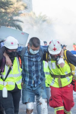 Santiago de Chile - Şili, 25-11-2019: Ekose gömlekli bir adama diğer iki adam yardım ediyor. Adamlardan biri sarı yelek giyiyor.