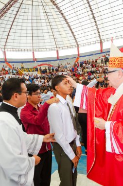 Tumbes, Tumbes, Peru 21-10-2023, Doğrulama Ayini: Bir rahip genç bir adamın kafasına dokunuyor. Rahip kırmızı bir bornoz giyiyor. Genç adam beyaz bir gömlek giyiyor.