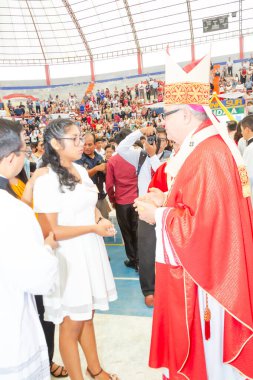 Tumbes, Tumbes, Peru 21-10-2023, Doğrulama Ayini: Kırmızı cüppeli bir adam beyaz elbiseli bir kadınla konuşuyor. Adam bir rahip ve kadın da genç bir kız. Sahne, büyük bir kalabalığın izlediği bir stadyumda geçiyor.