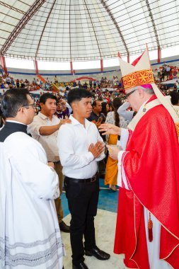 Tumbes, Tumbes, Peru 21-10-2023, Onaylama Ayini: Kırmızı cüppeli bir adam beyaz gömlekli bir adamı kutsuyor. Arka planda başkaları da var.