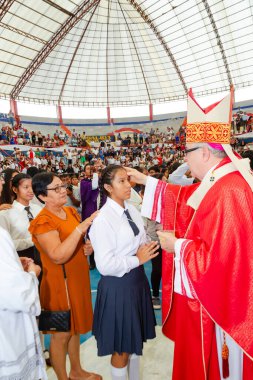 Tumbes, Tumbes, Peru 21-10-2023, Doğrulama Ayini: Kırmızı cüppeli bir adam bir kızın alnına dokunuyor. Kız beyaz bir gömlek ve mavi bir etek giyiyor. Bu adam bir rahip.