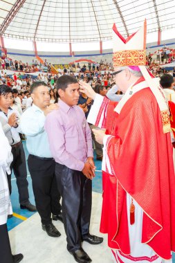 Tumbes, Tumbes, Peru 21-10-2023, Onaylama Ayini: bir adam bir rahip tarafından kutsandı. Rahip kırmızı bir bornoz ve beyaz bir şapka giyiyor. Kutsanmış adam beyaz gömlek ve siyah pantolon giyiyor. Arka planda bir sürü insan var.