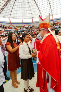 Tumbes, Tumbes, Peru 21-10-2023, Doğrulama Ayini: Kırmızı cüppeli bir adam bir kızı kutsuyor. Kız beyaz gömlek ve kahverengi etek giyiyor.
