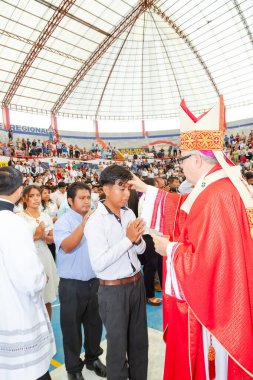 Tumbes, Tumbes, Peru 21-10-2023, Onaylama Ayini: Bir rahip kırmızı cüppeli genç bir adamı kutsar. Rahip beyaz bir bornoz giyiyor ve bir kalabalık tarafından çevrili. Genç adam, rahip tarafından kutsandı, şu anda...