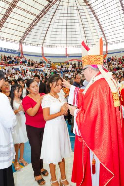 Tumbes, Tumbes, Peru 21-10-2023, Doğrulama Ayini: Kırmızı cüppeli bir adam bir kadının kafasına dokunuyor. Kadın beyaz bir elbise giyiyor. Bu adam bir rahip.