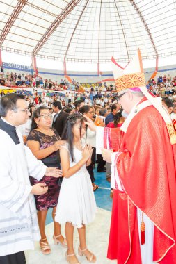 Tumbes, Tumbes, Peru 21-10-2023, Doğrulama Ayini: Bir rahip genç bir kızı kutsuyor. Rahip kırmızı bir bornoz giyiyor ve kız beyaz bir elbise giyiyor. Rahibin etrafı bir grup insanla çevrili.