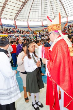 Tumbes, Tumbes, Peru 21-10-2023, Doğrulama Ayini: Kırmızı cüppeli bir adam bir kızı kutsuyor. Kız diz çöküyor ve adam onun kafasına dokunuyor. Arka planda bir sürü insan var, bazıları beyaz gömlek giyiyor.