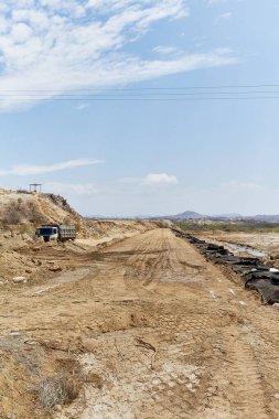 Birkaç aracı ve kamyonu olan toprak bir yol. Yol boş ve gökyüzü temiz.