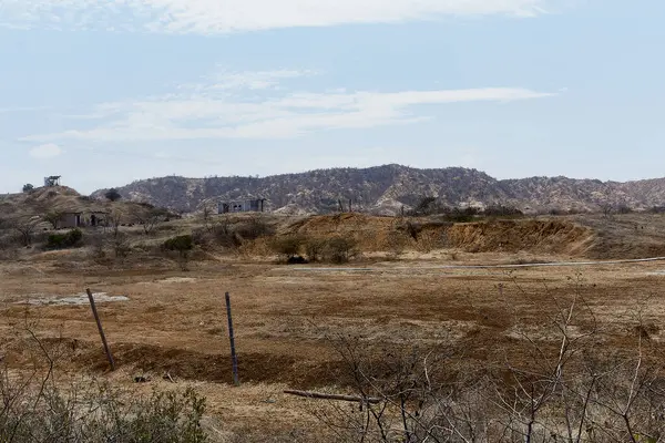 Önünde çit olan kuru, çorak bir tarla. Gökyüzü açık ve güneş parlıyor.