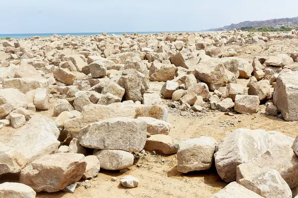 Önünde büyük bir kaya yığını olan kayalık bir sahil. Kumsal boş ve kayalar her yere dağılmış.