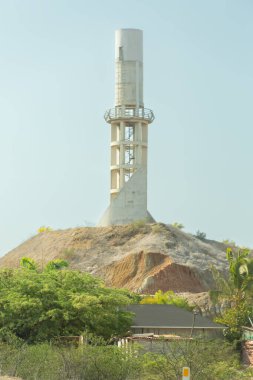 Arkasında yeşil bir tepe olan uzun beyaz bir kule. Tepe ağaçlarla kaplı ve kule bir ormanla çevrili.