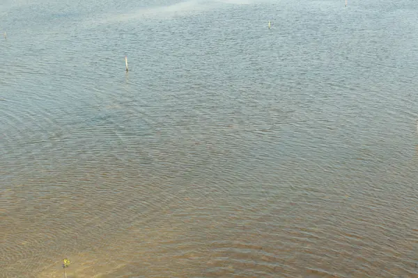 Su sakin ve hareketsiz, yüzeyde dalgalanmalar oluşuyor. Gökyüzü berrak ve mavi, ve su açık mavi bir renk gibi görünüyor.