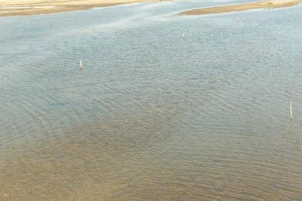 Su sakin ve durgun, birkaç küçük dalgalanmayla. Gökyüzü berrak ve mavi, ve su açık mavi bir renktir.