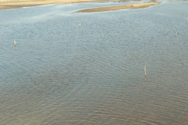 Su sakin ve durgun, birkaç küçük dalgayla. Gökyüzü berrak ve mavi, ve su açık mavi bir renktir.
