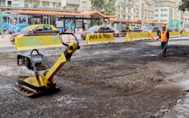 Santiago de Chile, Şili, 04-02-2021: Turuncu yelekli bir adam sarı bir makineyle yola püskürtüyor. Yol ıslak ve adam üzerine su püskürtüyor..