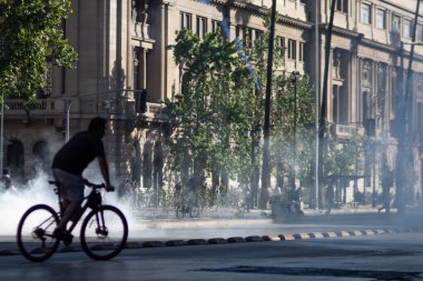 Santiago de Chile, Şili, 20-10-2019: Arka planda duman olan bir adam bisiklet sürüyor. Sahne biraz uğursuz ve öngörülü..