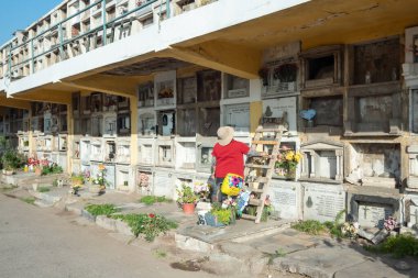 Santiago de Chile, Şili, 25-05-2021: Bir kadın mezarlığın önünde duruyor, çiçeklere bakıyor. Mezarlık mezar taşlarıyla dolu ve kadın çiçeklere bakıyor..