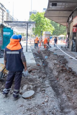 Santiago de Chile - Şili, 27-06-2021: Mavi yelek ve turuncu şapkalı bir adam bir inşaat alanının yanında kaldırımda duruyor.